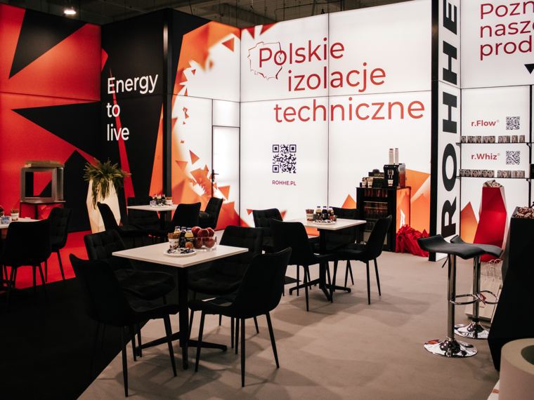 Stoliki na stoisku ROHHE między ścianą Energy to live a regałem produktowym